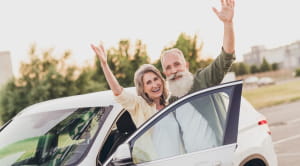 Man and woman waving outside of their car